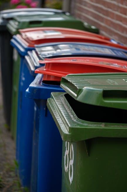 A view of a driveway or paved outdoor area contains a large pile of discarded household or office rubbish, primarily composed of cardboard boxes, plastic containers, and various packaging materials. T