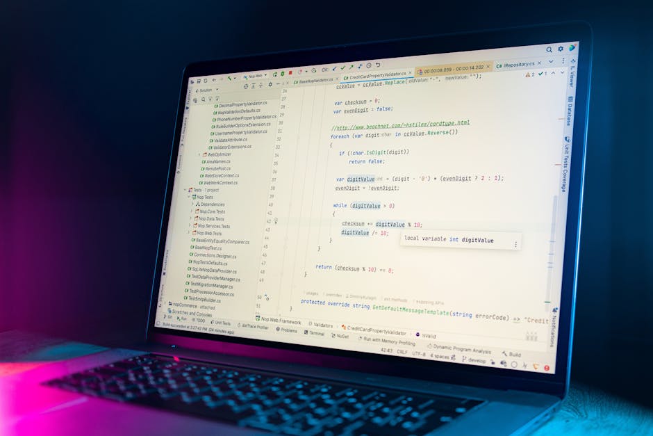 This image features an open laptop placed on a wooden table, displaying lines of code or script on its screen. The laptop has a silver or metallic finish with a dark keyboard, and a slim profile. To t